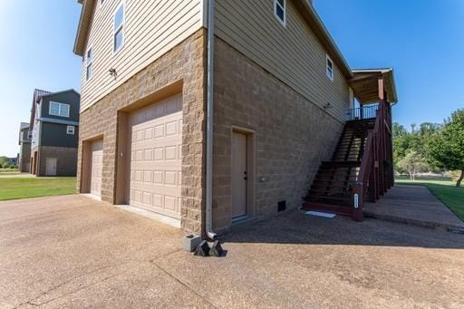 view of side of home with a garage, stone siding, stairway, and driveway