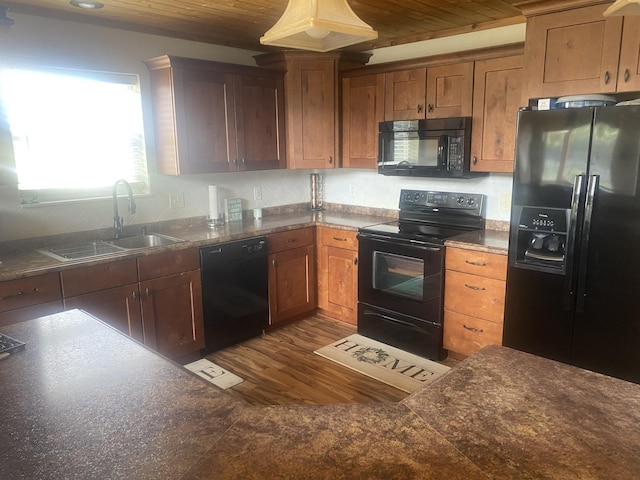 kitchen featuring dark wood-type flooring, a sink, decorative backsplash, black appliances, and dark countertops