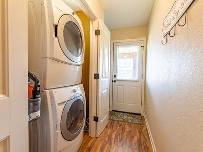 clothes washing area with stacked washer and dryer, a textured wall, wood finished floors, laundry area, and baseboards