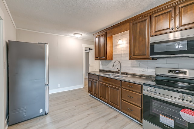 kitchen featuring light wood-type flooring, backsplash, appliances with stainless steel finishes, sink, and a textured ceiling