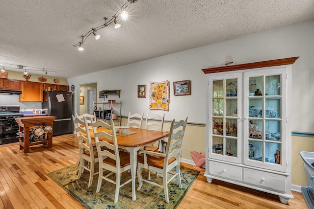 dining area featuring a textured ceiling, light hardwood / wood-style floors, and rail lighting