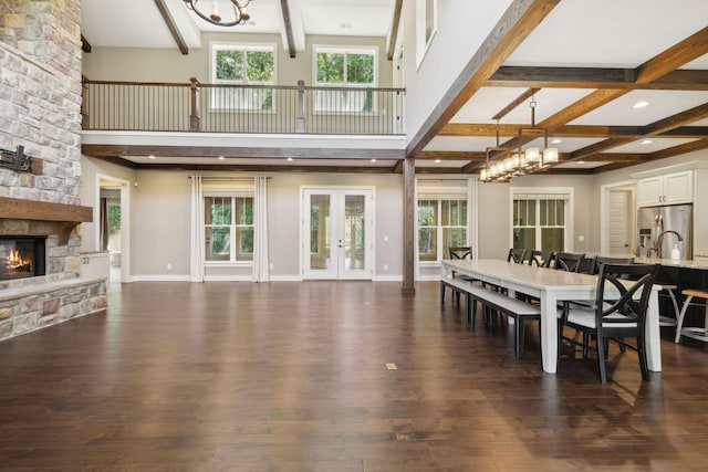 dining space featuring a stone fireplace, a chandelier, dark wood-style flooring, and french doors