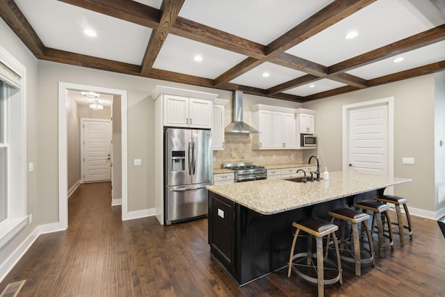 kitchen featuring a spacious island, appliances with stainless steel finishes, white cabinets, wall chimney range hood, and a kitchen bar