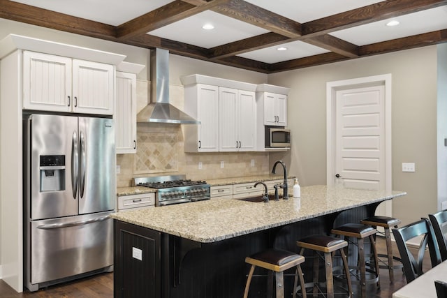 kitchen featuring a center island with sink, stainless steel appliances, white cabinets, a sink, and wall chimney exhaust hood