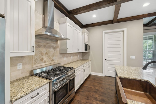 kitchen with light stone counters, a sink, white cabinets, appliances with stainless steel finishes, and wall chimney exhaust hood