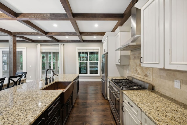 kitchen with light stone counters, a sink, white cabinetry, appliances with stainless steel finishes, and wall chimney exhaust hood