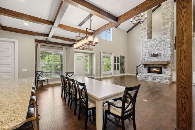 dining space with dark wood-style flooring, beamed ceiling, a stone fireplace, and an inviting chandelier