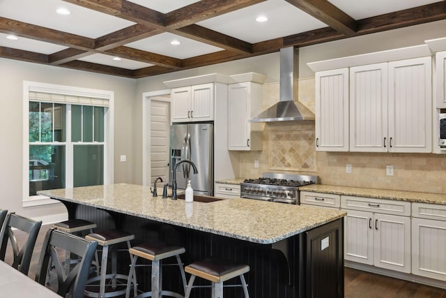 kitchen featuring wall chimney range hood, appliances with stainless steel finishes, a kitchen bar, and a center island with sink