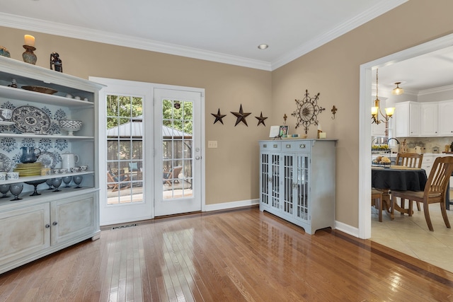 dining space with sink, light wood-type flooring, a notable chandelier, and ornamental molding