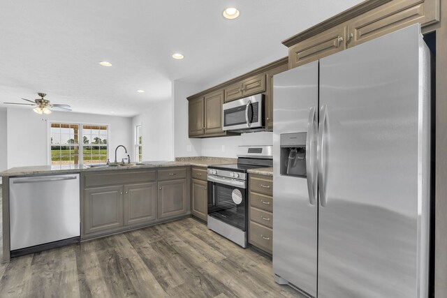 kitchen featuring ceiling fan, dark hardwood / wood-style flooring, appliances with stainless steel finishes, light stone countertops, and kitchen peninsula