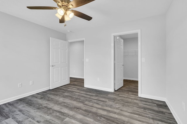 unfurnished bedroom with a walk in closet, a closet, ceiling fan, and dark hardwood / wood-style floors