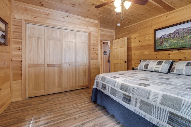 bedroom with a closet, light hardwood / wood-style floors, ceiling fan, wooden walls, and wood ceiling