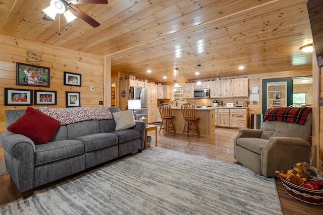 living room with light hardwood / wood-style flooring, wood ceiling, wood walls, sink, and ceiling fan