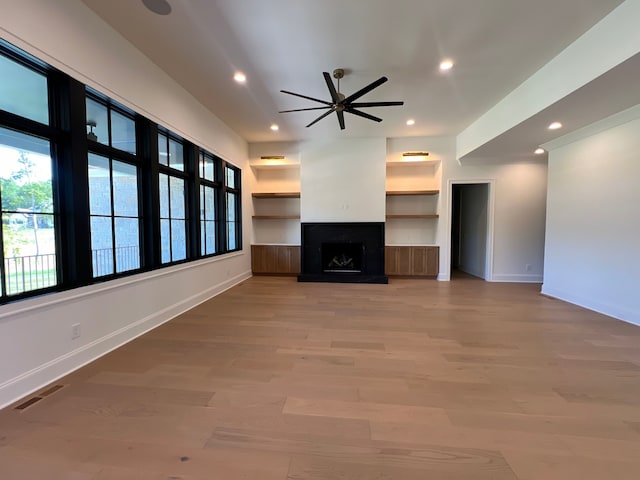 unfurnished living room with wood-type flooring, ceiling fan, and built in shelves