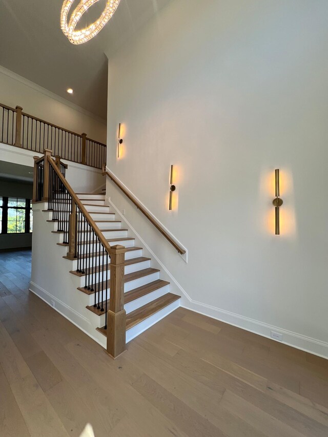 staircase featuring wood-type flooring, ornamental molding, and a chandelier