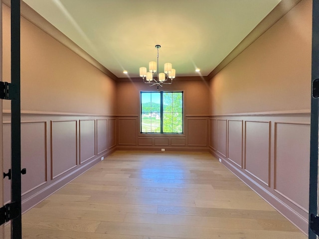 empty room with ornamental molding, light wood-style floors, an inviting chandelier, wainscoting, and a decorative wall