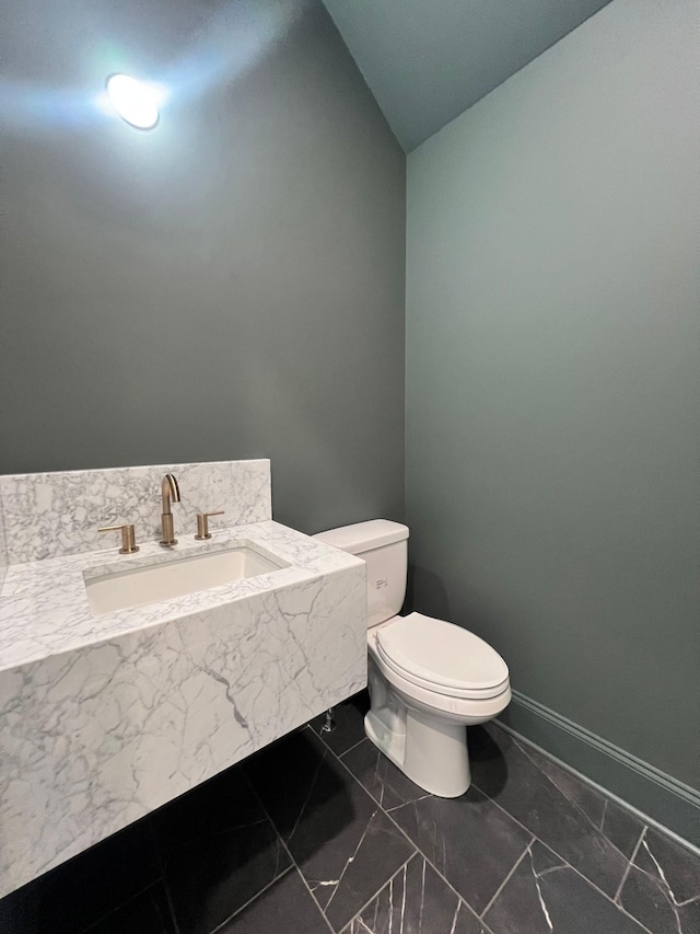 bathroom featuring baseboards, toilet, lofted ceiling, and a sink