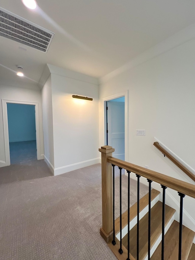 hall with visible vents, baseboards, carpet, and an upstairs landing