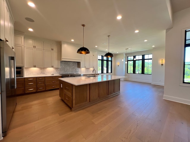 kitchen with premium range hood, sink, high quality fridge, a kitchen island with sink, and decorative backsplash