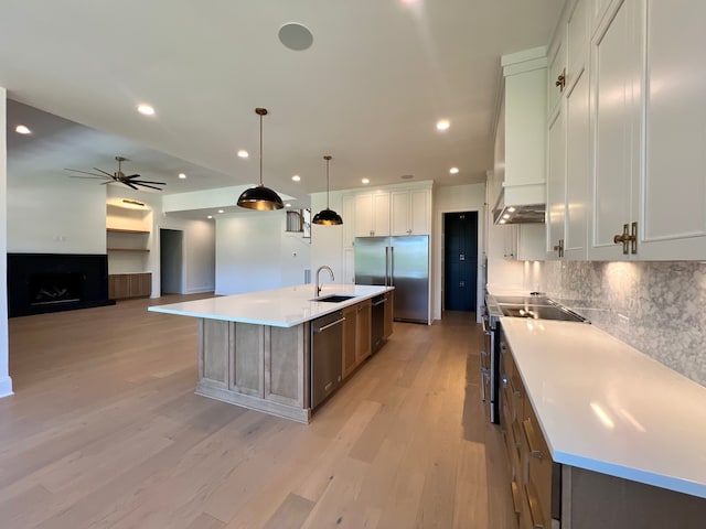 kitchen featuring light hardwood / wood-style flooring, a large island with sink, pendant lighting, stainless steel appliances, and white cabinets