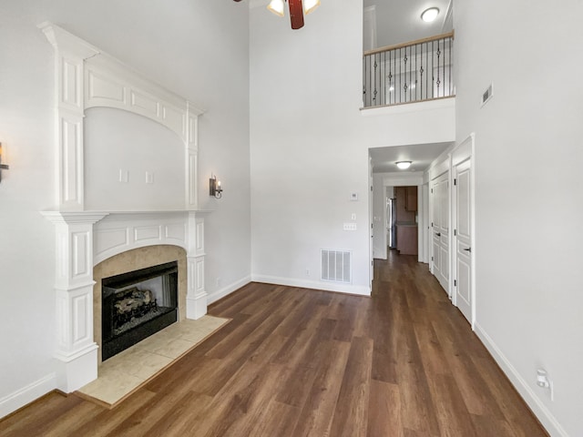 unfurnished living room featuring a high ceiling, ceiling fan, hardwood / wood-style flooring, and a tile fireplace