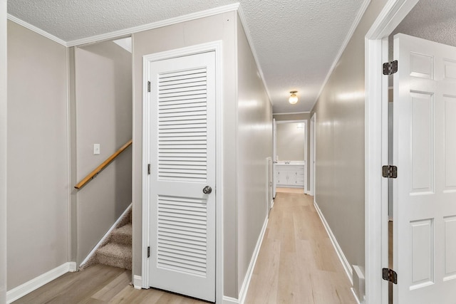 corridor featuring light wood finished floors, baseboards, ornamental molding, stairs, and a textured ceiling