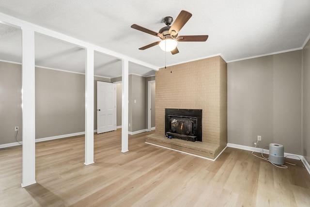 unfurnished living room with ornamental molding, a brick fireplace, a textured ceiling, wood finished floors, and baseboards