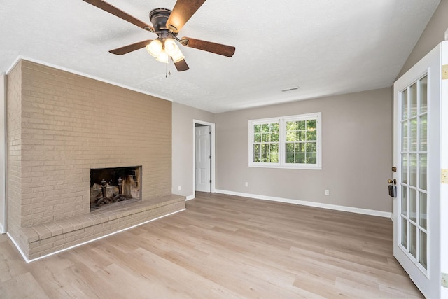 unfurnished living room with a brick fireplace, baseboards, a textured ceiling, and light wood finished floors