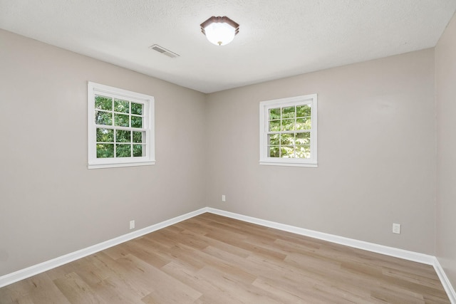 spare room featuring light wood-type flooring, visible vents, and baseboards