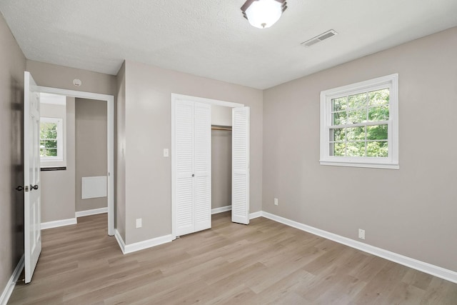 unfurnished bedroom featuring visible vents, baseboards, light wood-style flooring, a textured ceiling, and a closet