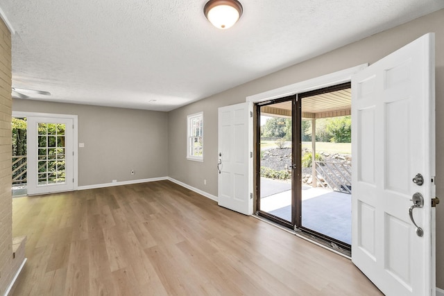 interior space with baseboards, a textured ceiling, and light wood finished floors