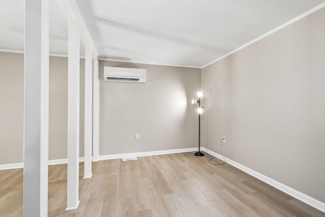 empty room with light wood-type flooring, an AC wall unit, a textured ceiling, and baseboards