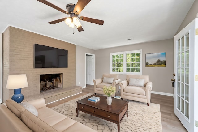 living room with baseboards, visible vents, ceiling fan, wood finished floors, and a brick fireplace