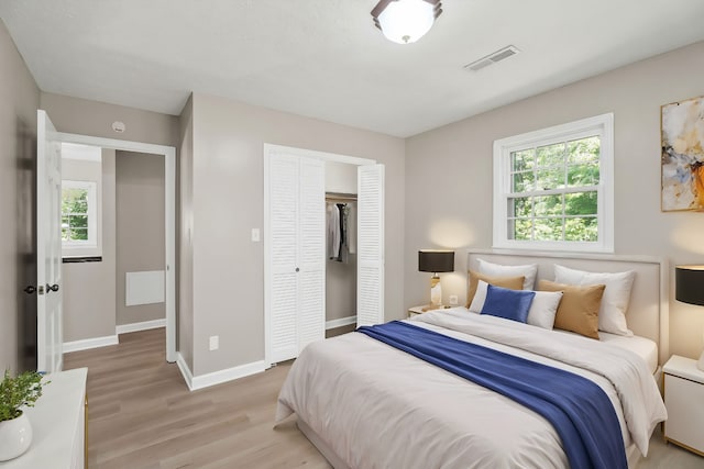 bedroom with light wood-type flooring, baseboards, visible vents, and a closet