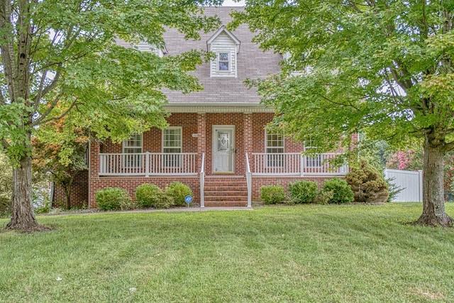 new england style home with a porch, a front lawn, and brick siding