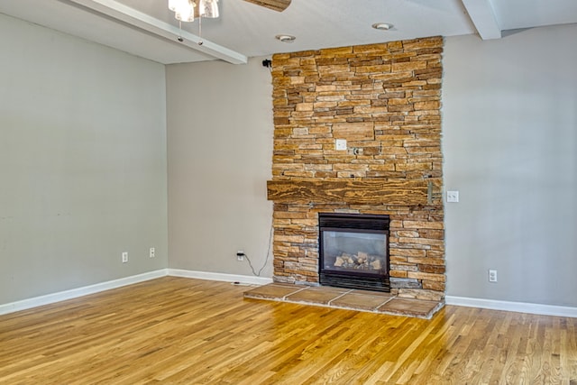 unfurnished living room with ceiling fan, beamed ceiling, wood-type flooring, and a fireplace