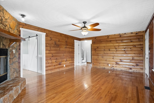 unfurnished living room featuring light hardwood / wood-style floors, a barn door, a stone fireplace, and ceiling fan