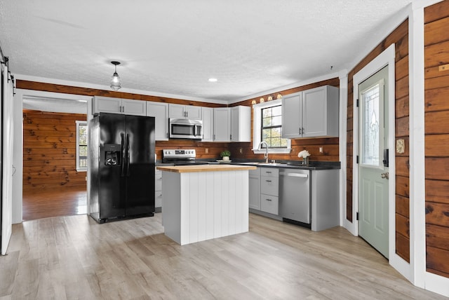 kitchen featuring appliances with stainless steel finishes, light hardwood / wood-style floors, gray cabinetry, wooden walls, and a kitchen island