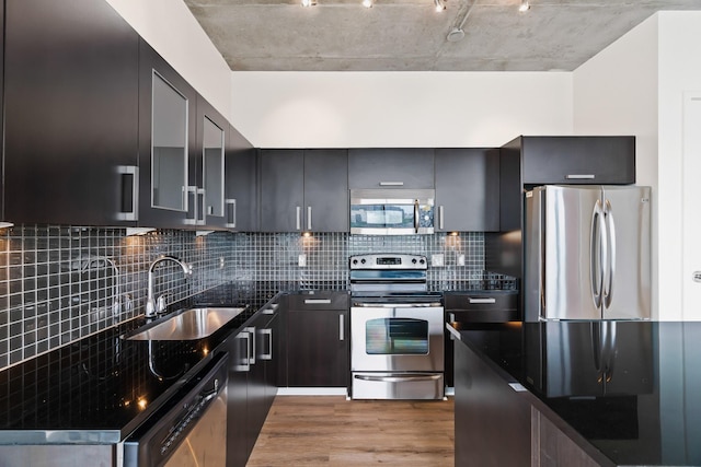 kitchen featuring dark stone countertops, a sink, decorative backsplash, stainless steel appliances, and light wood-style floors