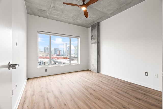 empty room with ceiling fan, baseboards, a city view, and wood finished floors