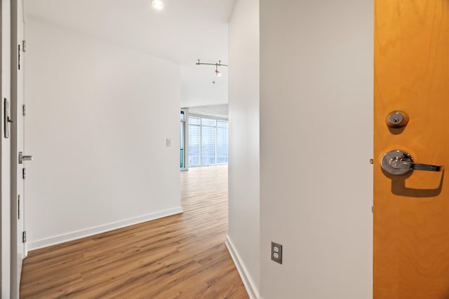 hallway featuring rail lighting, baseboards, wood finished floors, and floor to ceiling windows