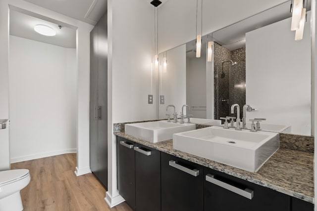 bathroom featuring wood finished floors, tiled shower, double vanity, and a sink