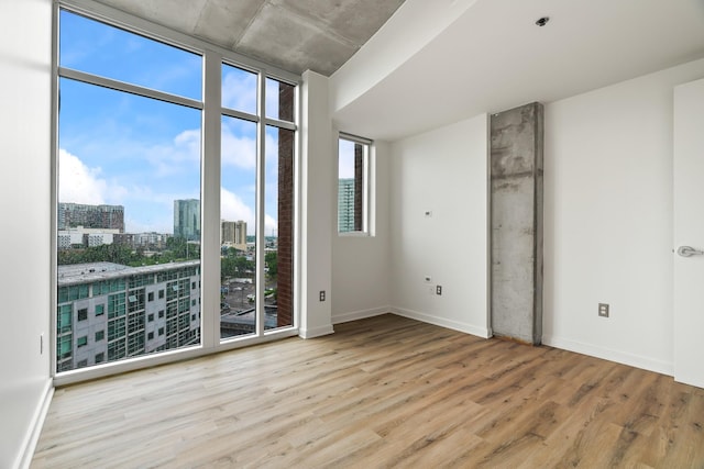 empty room with a wall of windows, baseboards, a city view, and wood finished floors