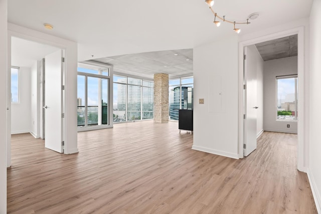 unfurnished living room with light wood-type flooring, baseboards, and floor to ceiling windows