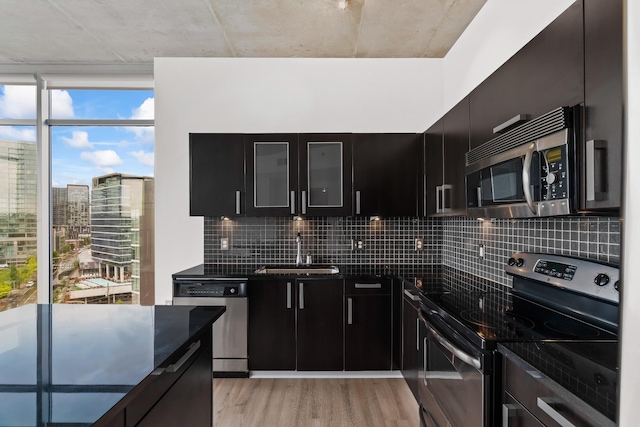 kitchen with a sink, backsplash, dark cabinetry, light wood-style floors, and appliances with stainless steel finishes