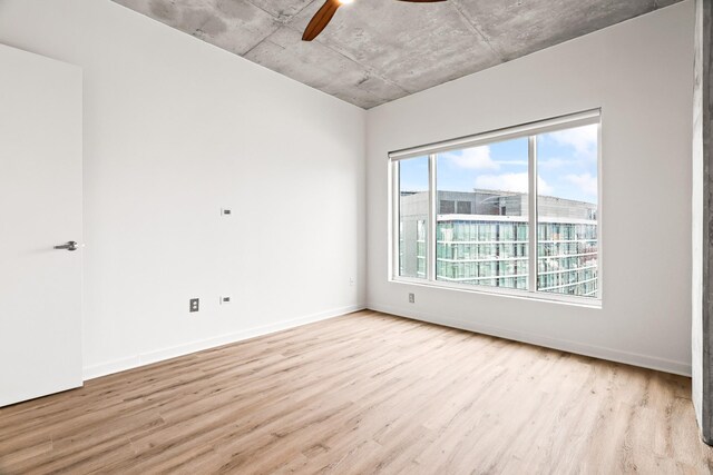 empty room featuring light wood-style flooring, a ceiling fan, and baseboards
