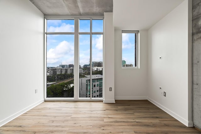 unfurnished room featuring baseboards, a view of city, wood finished floors, and floor to ceiling windows