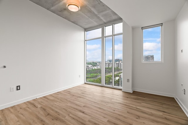 unfurnished room with a wall of windows, baseboards, light wood-style flooring, and a view of city