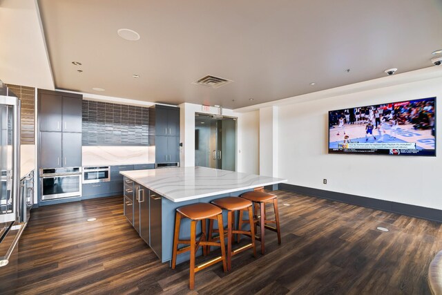 kitchen with dark hardwood / wood-style flooring, light stone counters, a kitchen island, a breakfast bar area, and oven