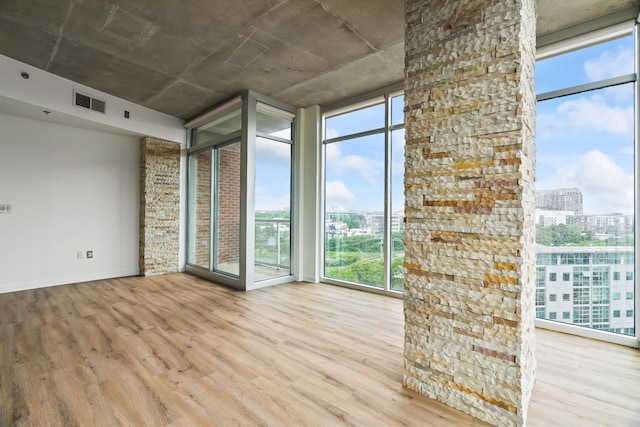 unfurnished room with wood finished floors, baseboards, visible vents, expansive windows, and a city view